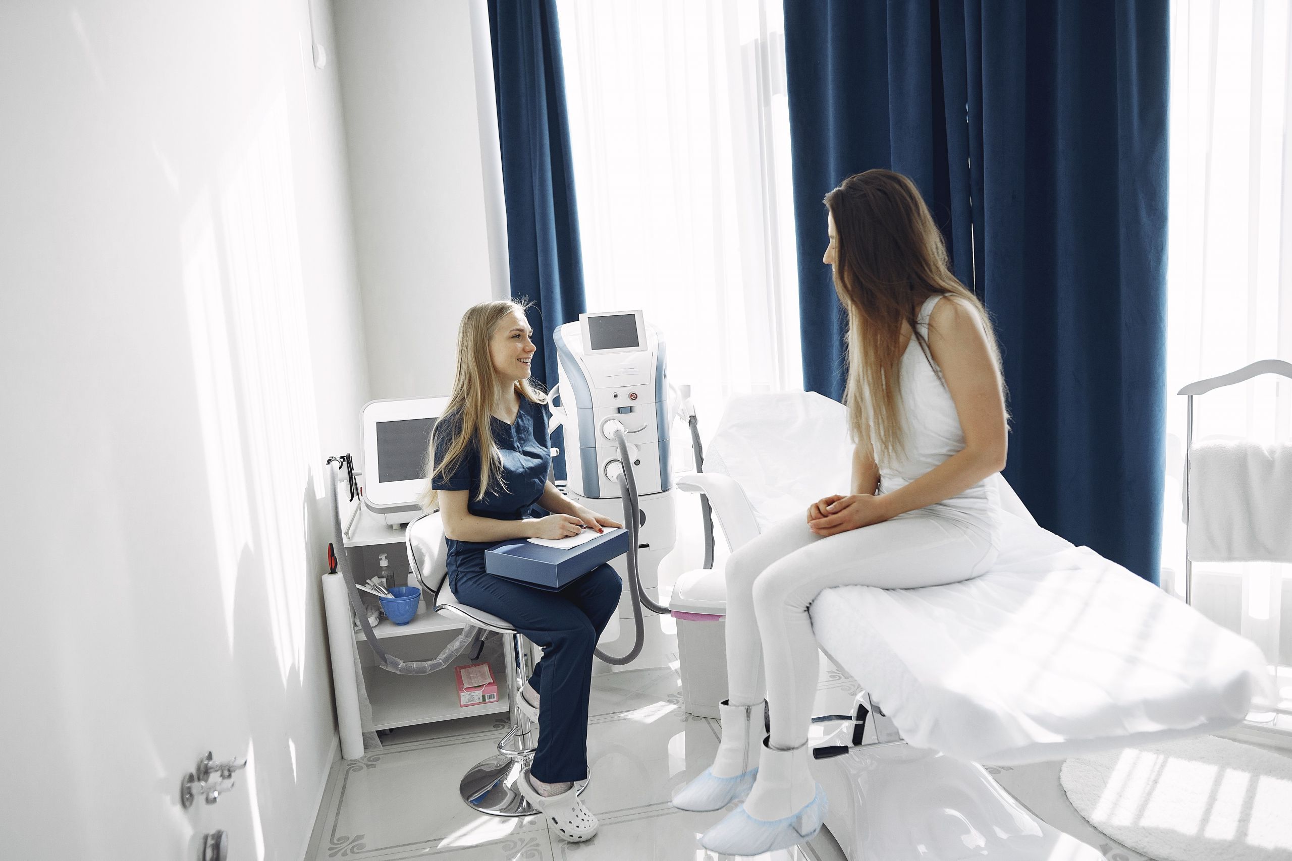 Woman in blue scrub suit helping woman sitting on bed