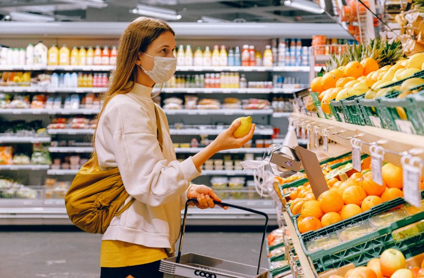 Woman in yellow tshirt and beige jacket holding a fruit stand