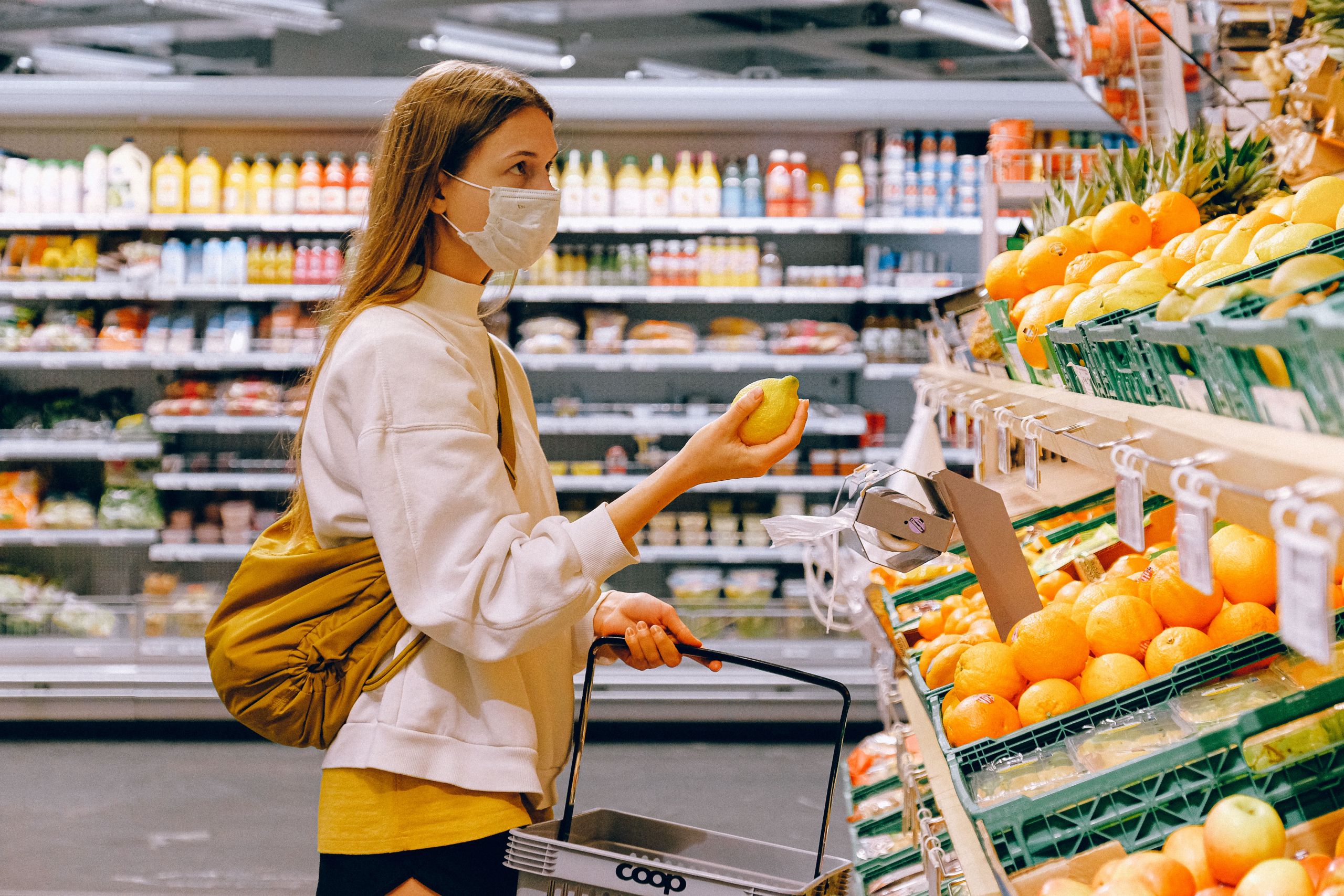 Woman in yellow tshirt and beige jacket holding a fruit stand